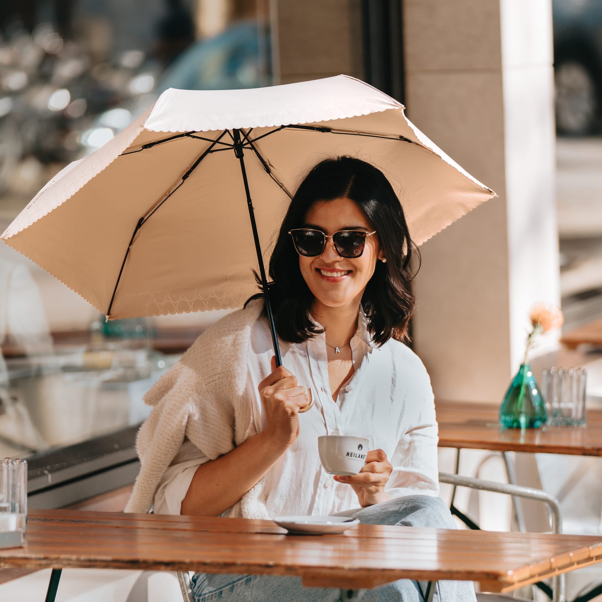 Frau mit Sunbarry Romantic Breezer Pearl Beige im Straßencafé – UV-Schutz beim Espresso in der Nachmittagssonne