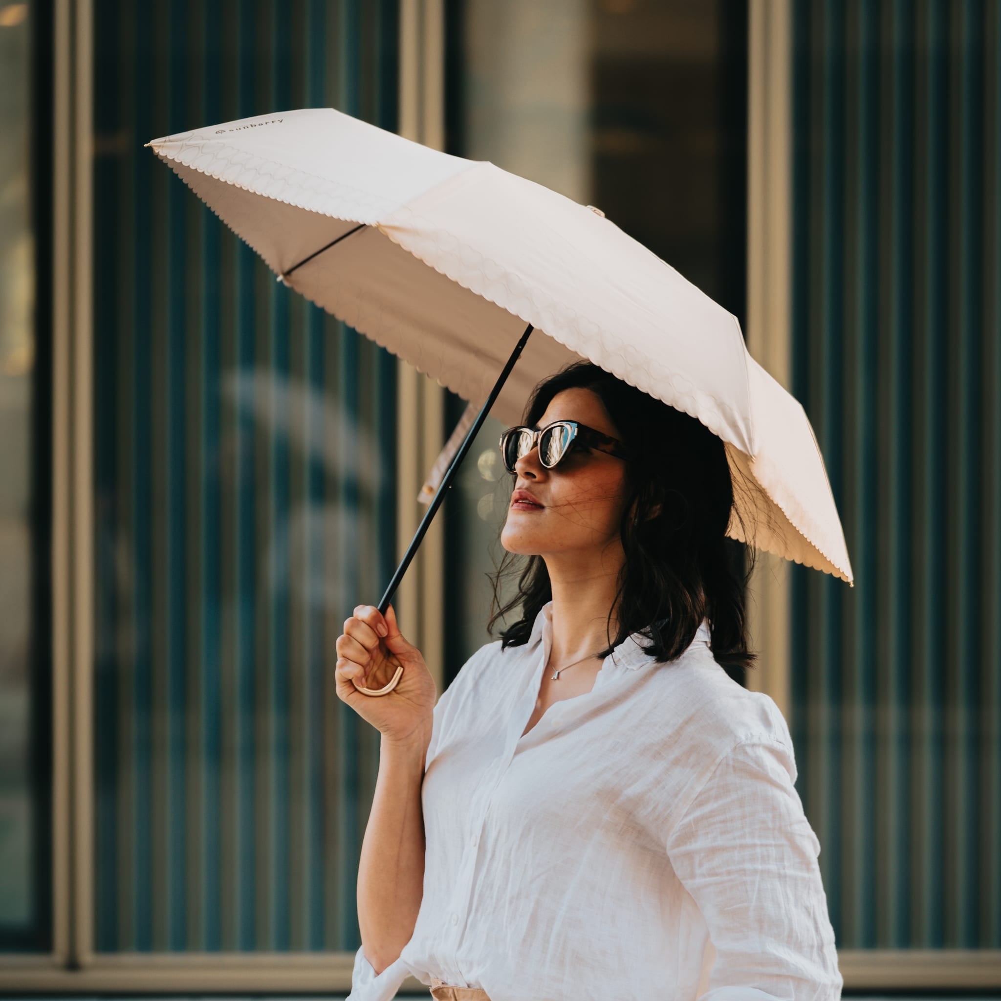 Frau mit Sunbarry Romantic Breezer Pearl Beige in der Stadt – UV-Schirm mit Herzbordüre und Goldgriff